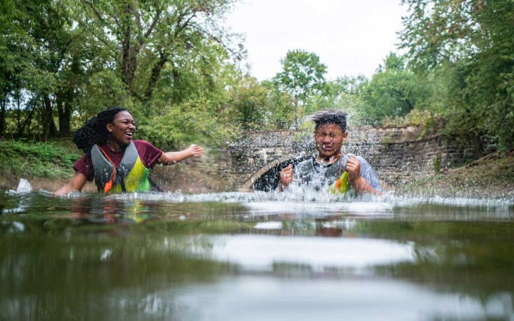 two teens splash each other in water on a canoeing trip with outward bound